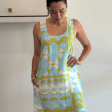 Woman wearing a blue and green patterned dress against a white wall.