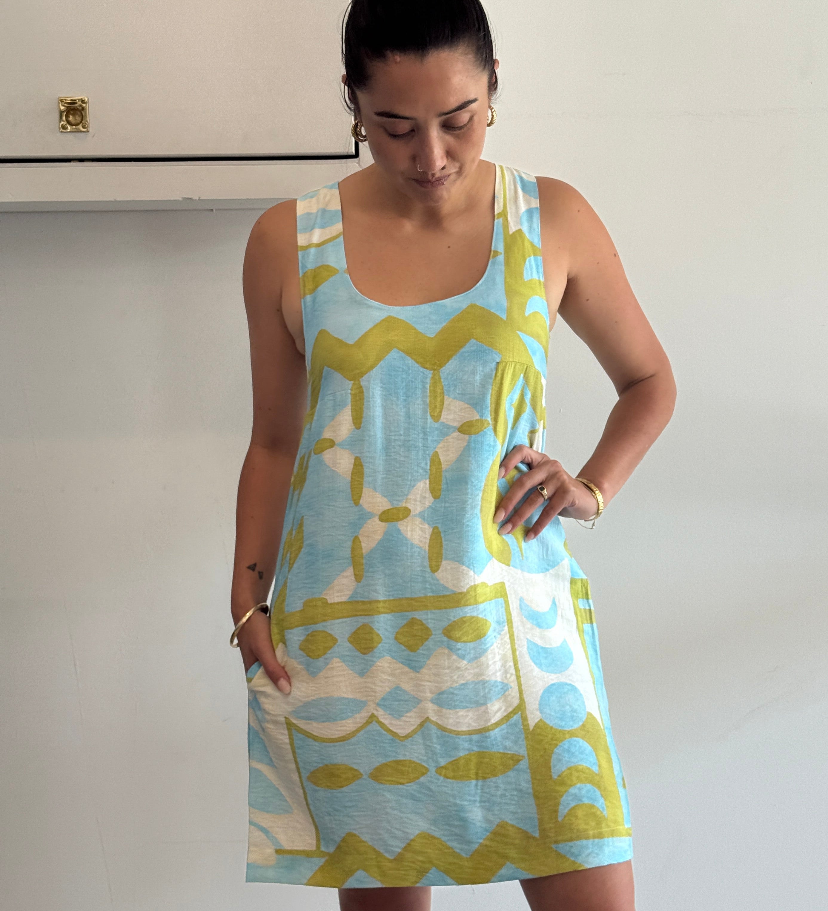 Woman wearing a blue and green patterned dress against a white wall.