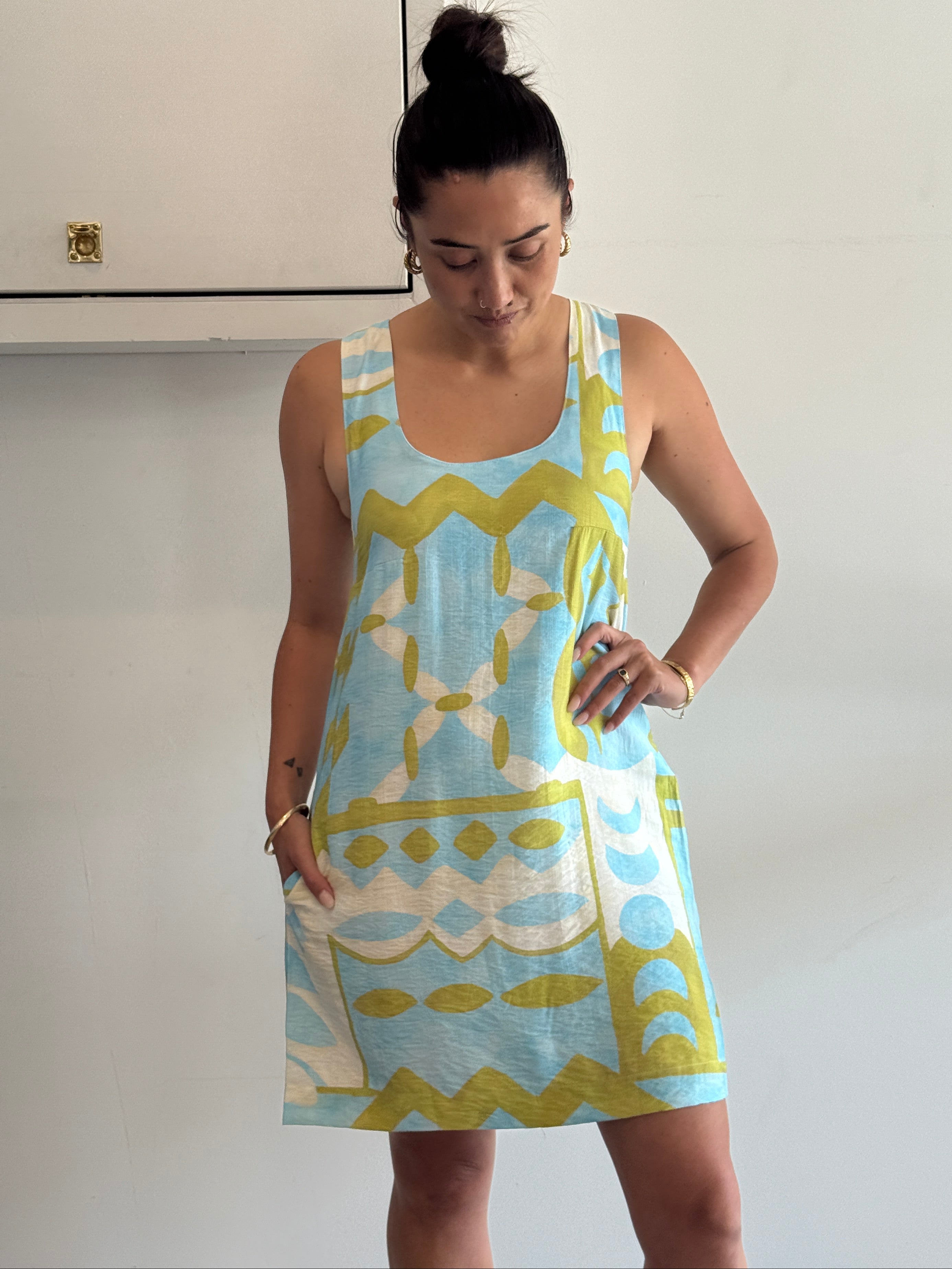 Woman wearing a blue and green patterned dress against a white wall.