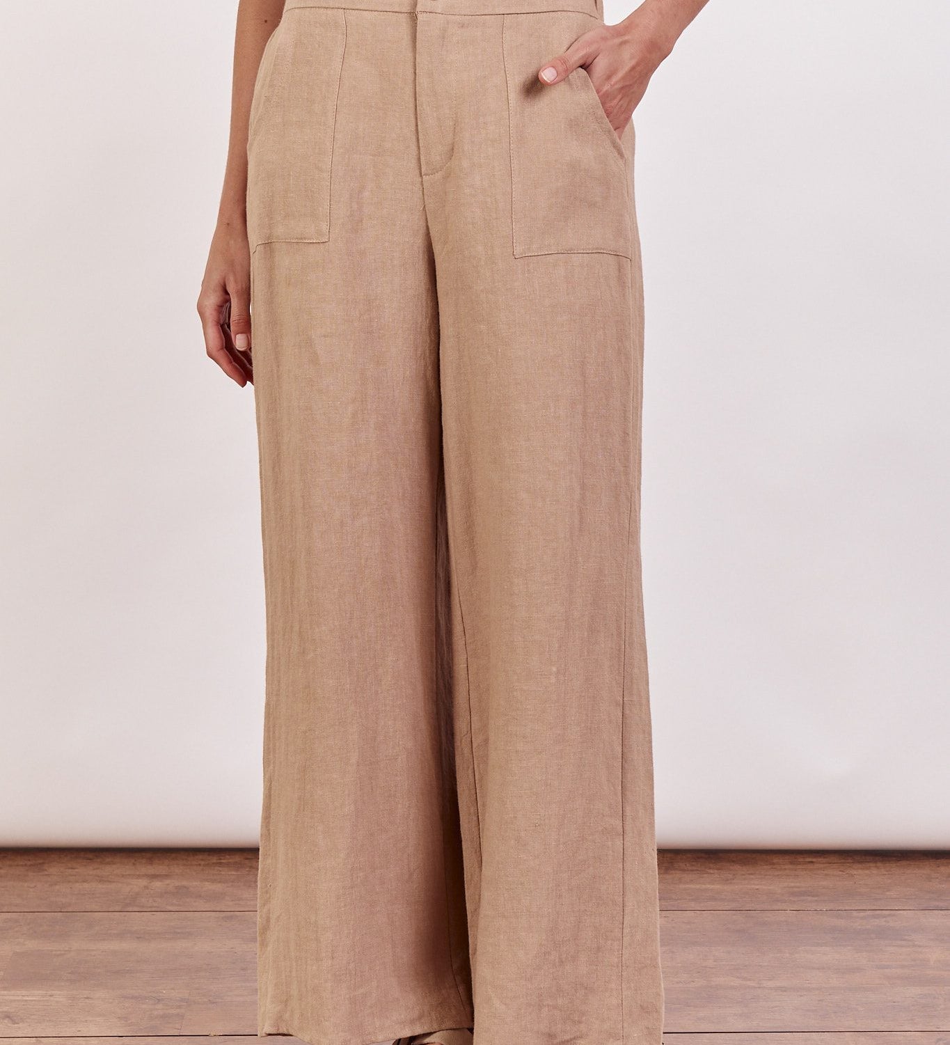 A woman standing in a taupe linen wide-leg pant with a white top, wearing flat sandals.