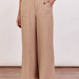 A woman standing in a taupe linen wide-leg pant with a white top, wearing flat sandals.