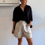 Person wearing a black shirt and beige shorts against a white wall.