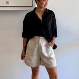 Person wearing a black shirt and beige shorts against a white wall.