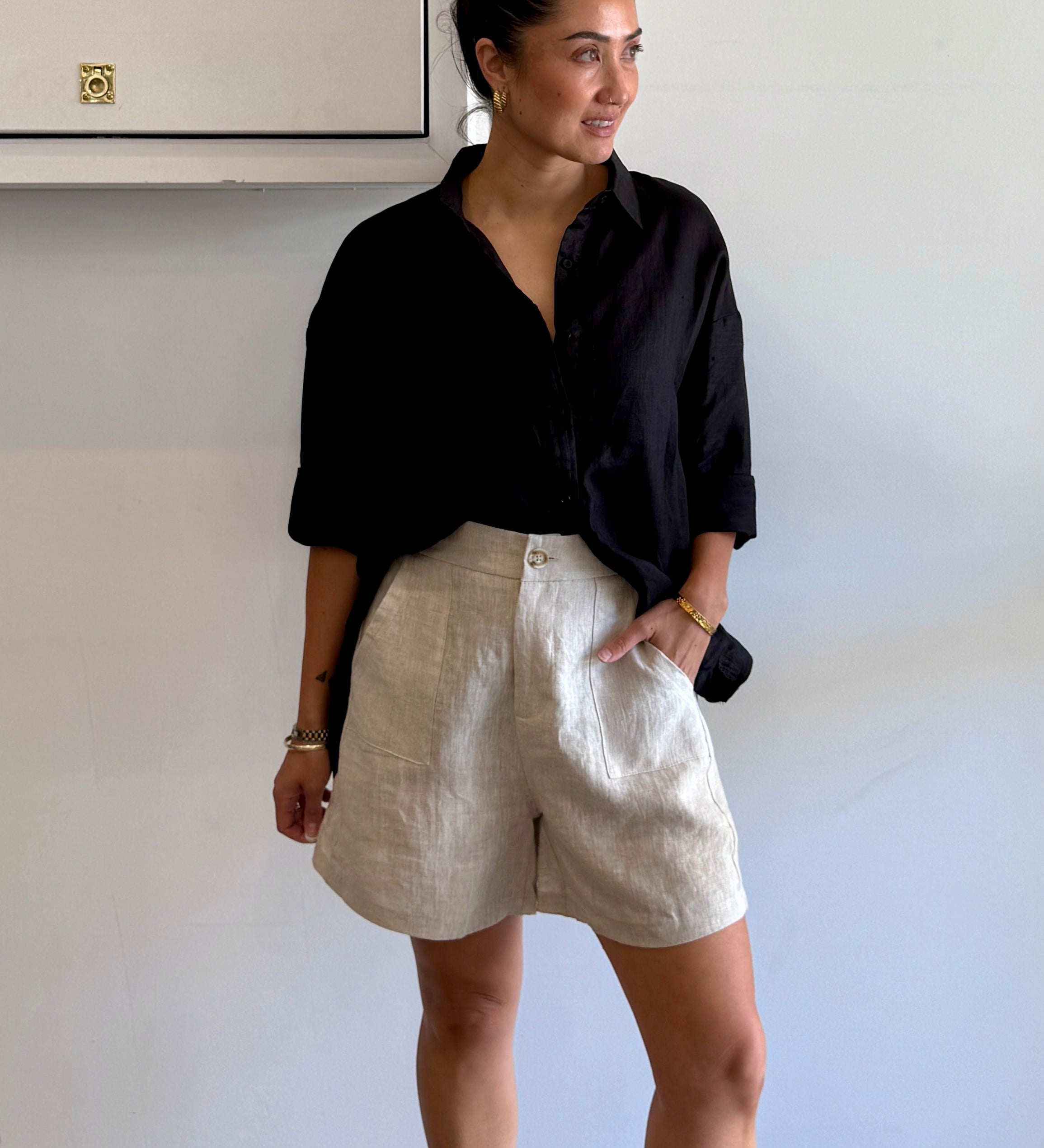 Person wearing a black shirt and beige shorts against a white wall.