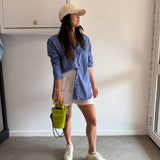 Person wearing a blue striped shirt and white shorts standing on a gray floor with a white wall.