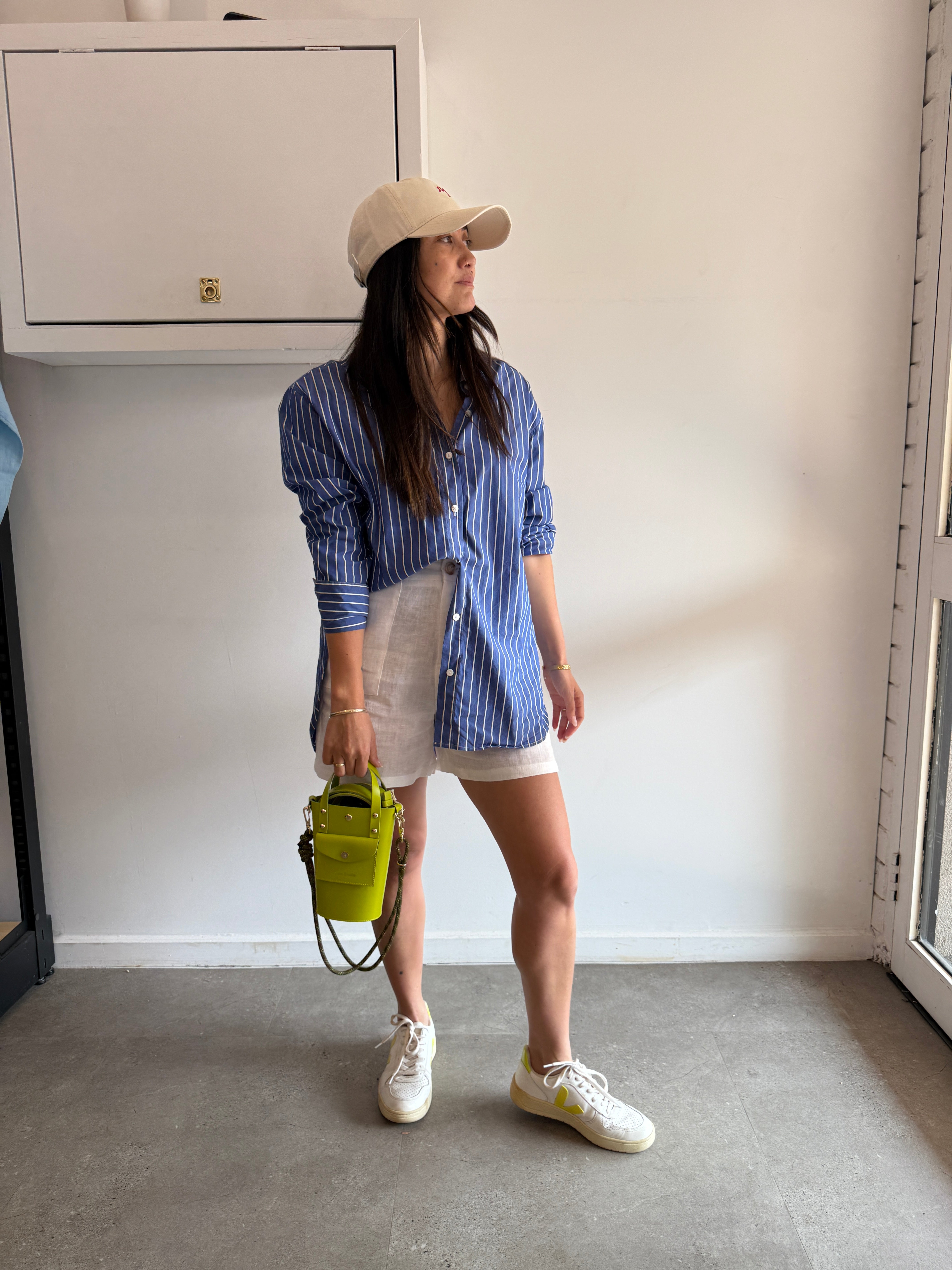 Person wearing a blue striped shirt and white shorts standing on a gray floor with a white wall.