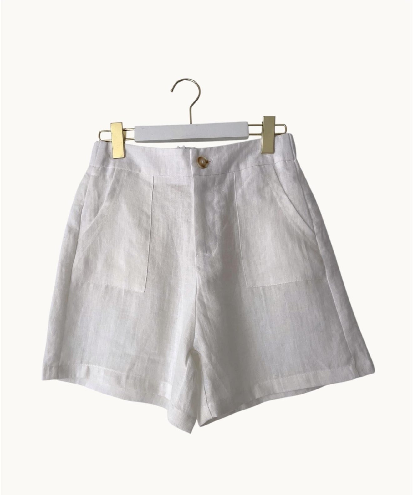 White linen shorts on a hanger against a white background