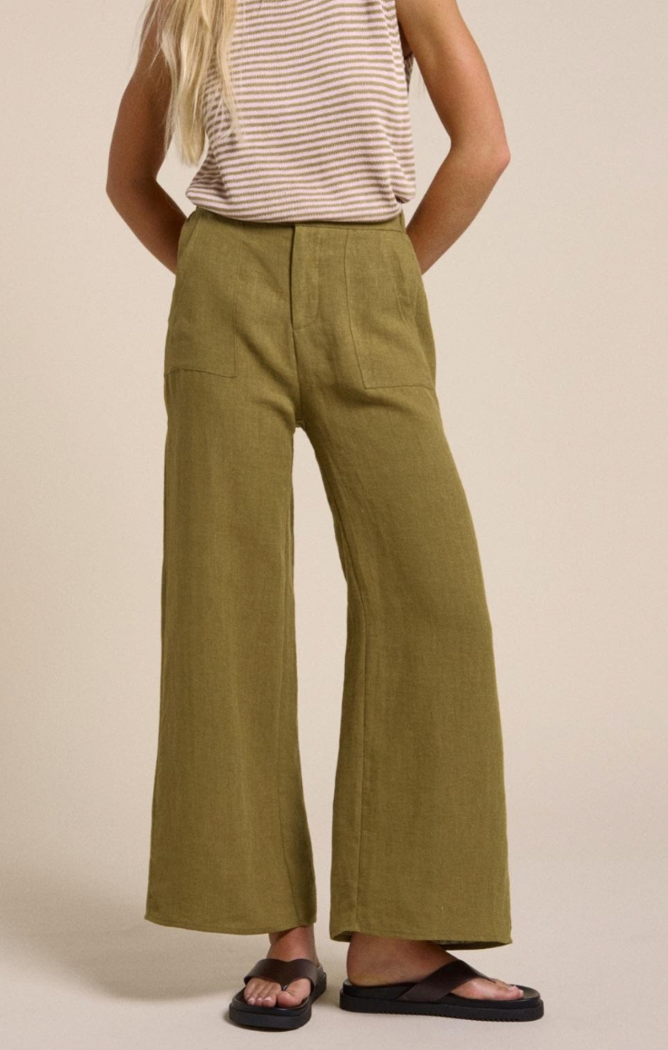 Person wearing olive green wide-leg Little Lies linen pants on a beige background