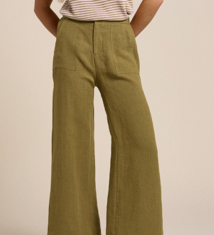 Person wearing olive green wide-leg Little Lies linen pants on a beige background