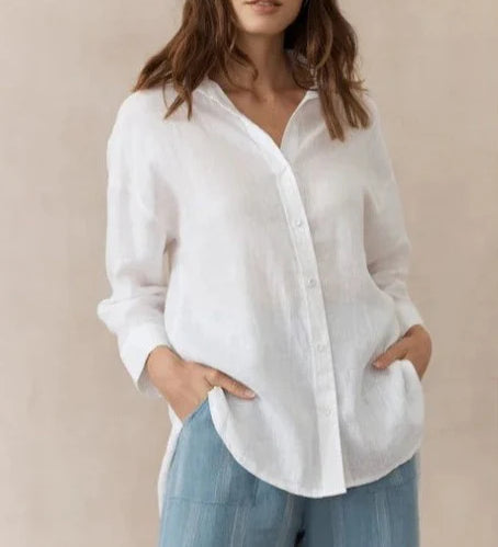 A woman wearing a white, collared, button-up shirt with cuffed sleeves and a high/low hemline, paired with blue denim pants.