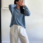 Woman wearing a blue sweater and white pants in an indoor setting