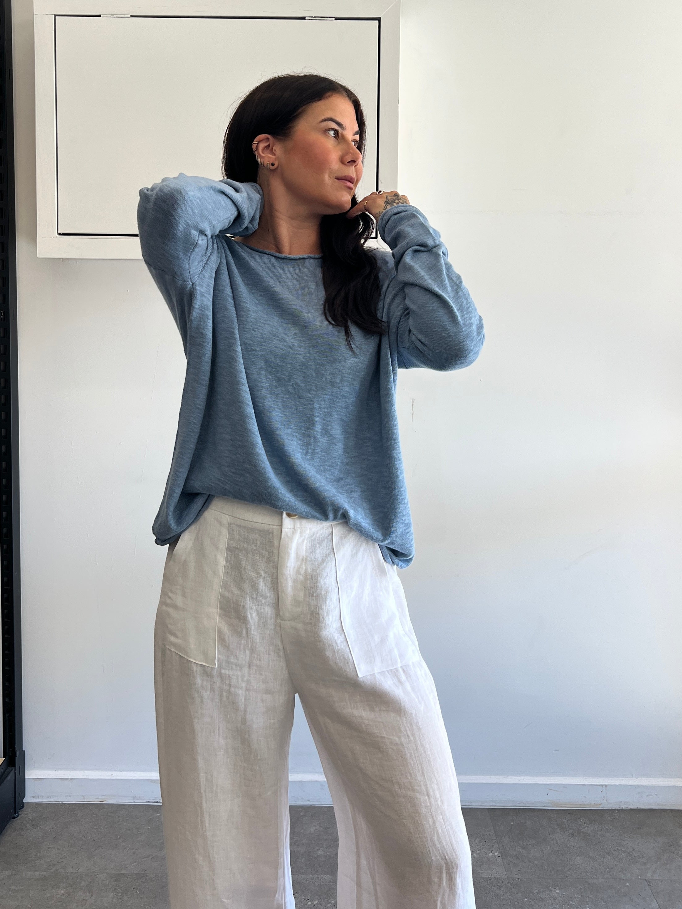 Woman wearing a blue sweater and white pants in an indoor setting