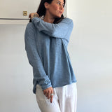 Woman wearing a blue hoodie and white pants against a white wall