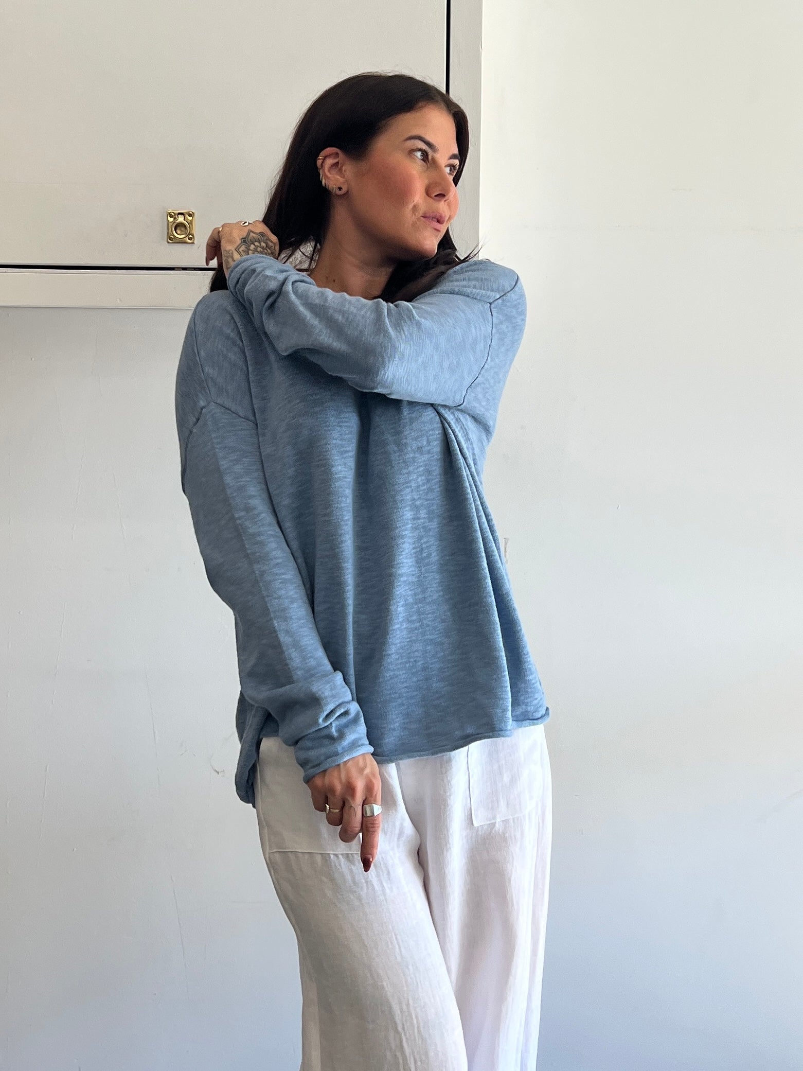 Woman wearing a blue hoodie and white pants against a white wall