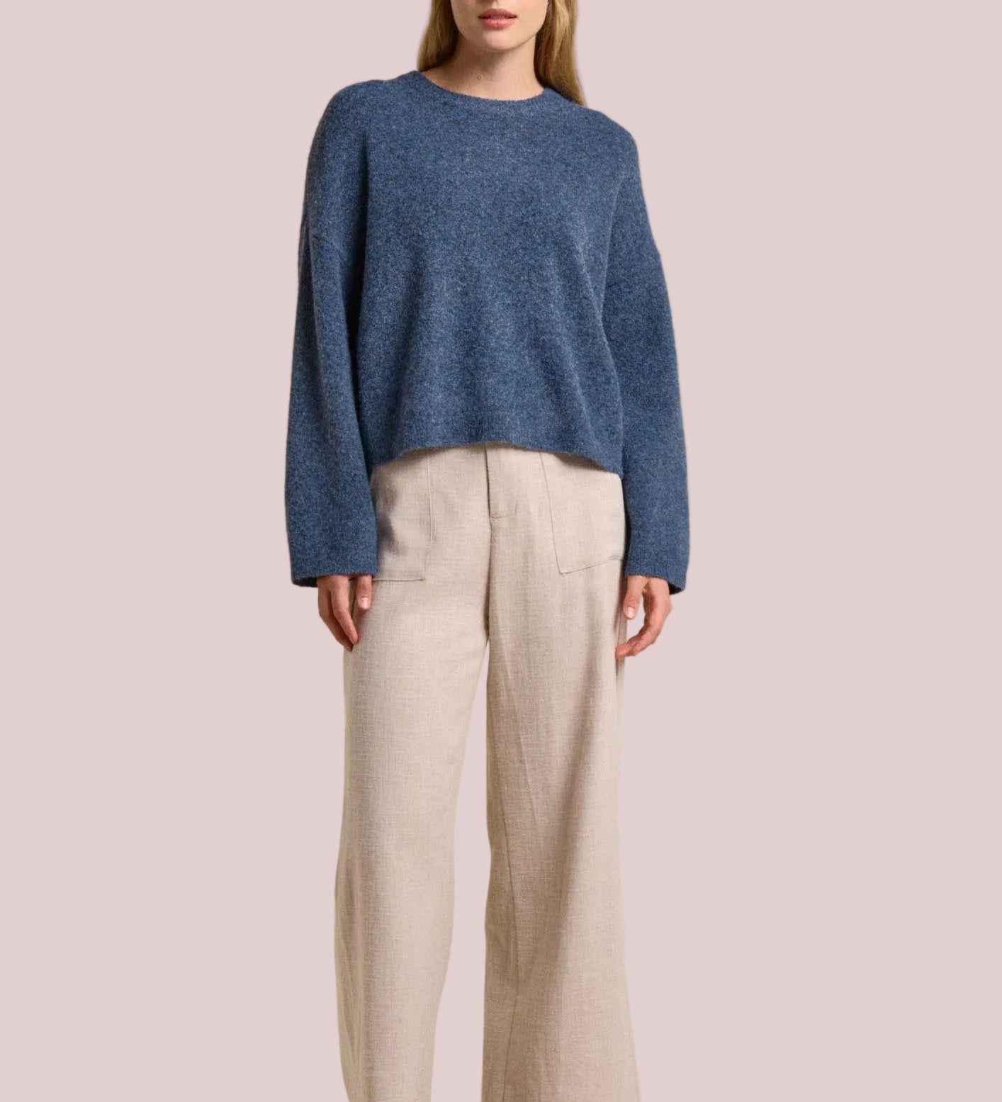Woman wearing a blue sweater and beige pants on a beige background