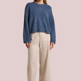 Woman wearing a blue sweater and beige pants on a beige background