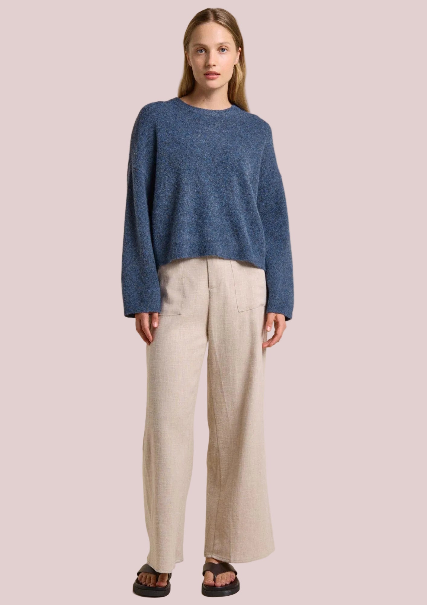 Woman wearing a blue sweater and beige pants on a beige background