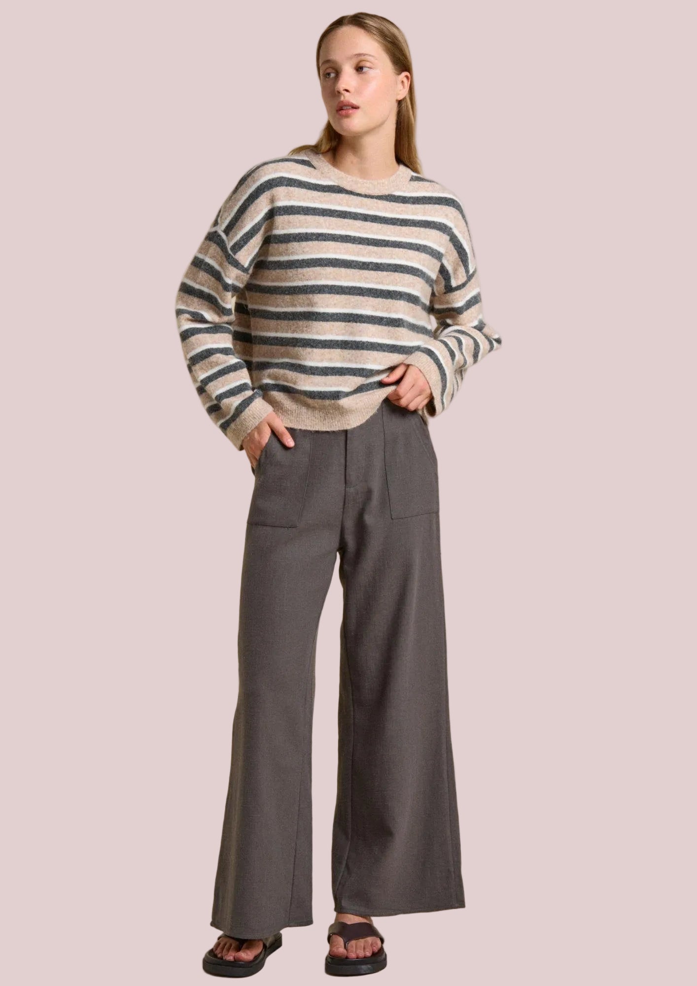 Woman wearing a striped sweater and gray pants on a beige background
