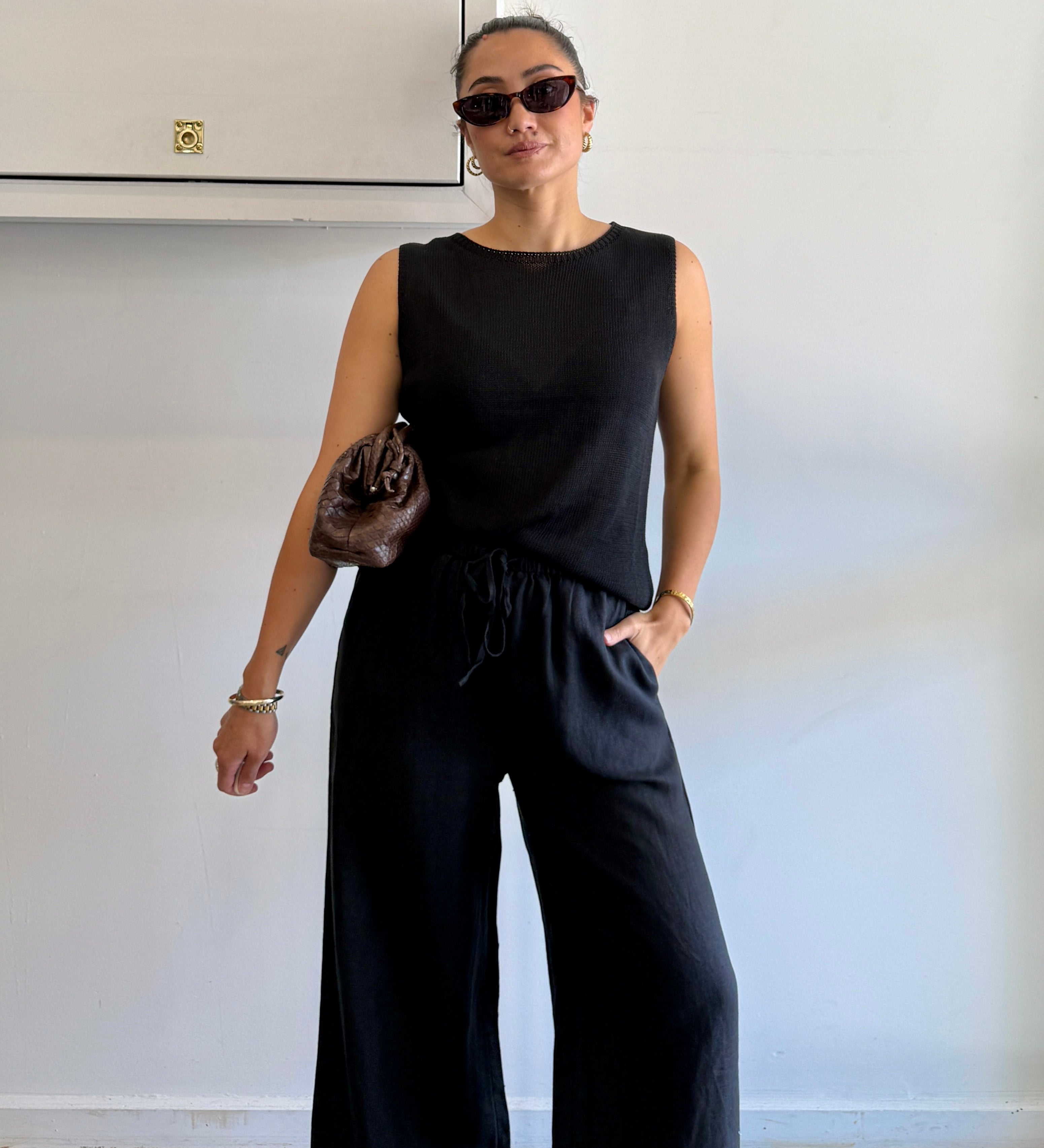 Woman wearing a black sleeveless top and wide-leg pants against a plain background