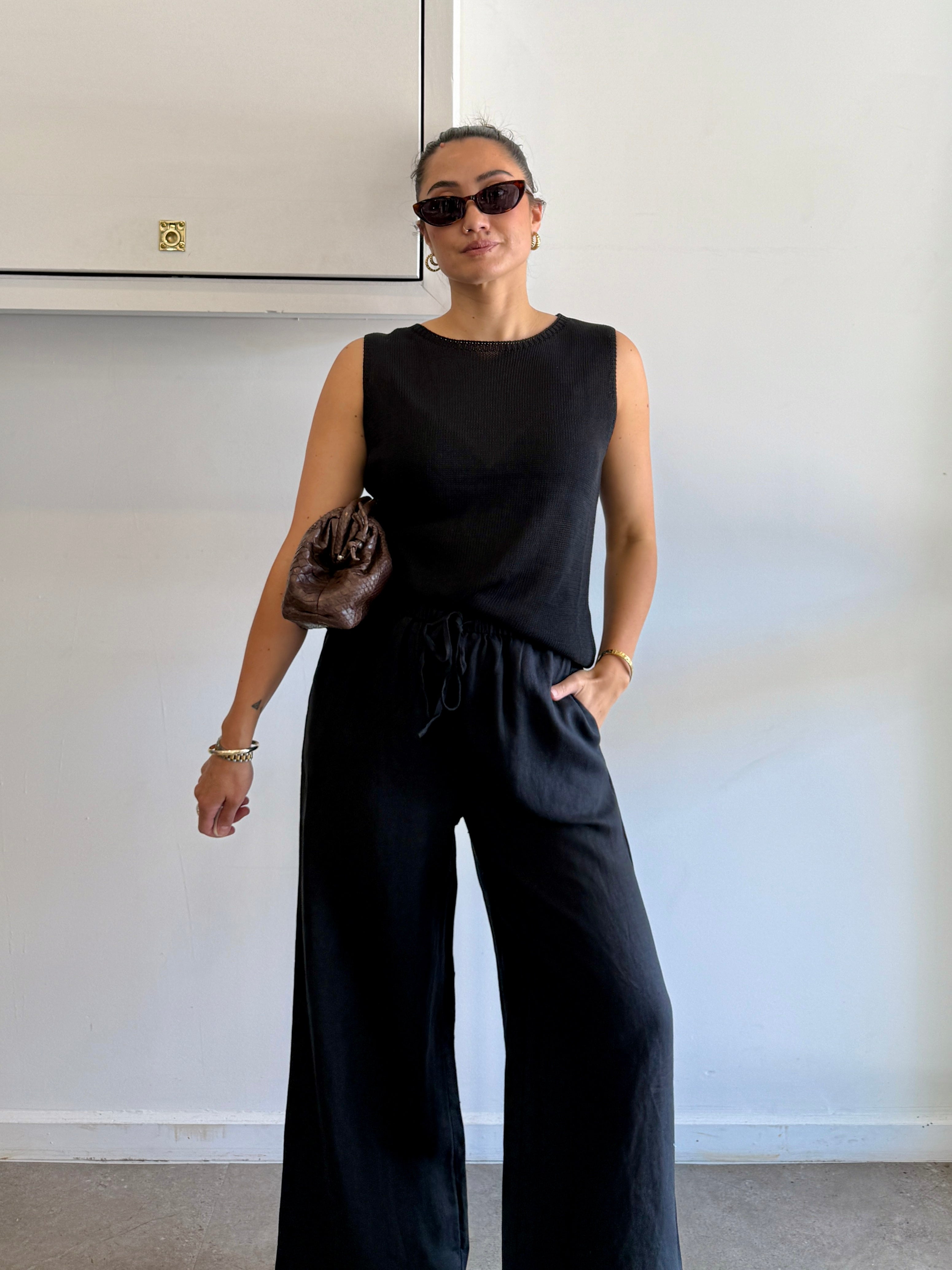 Woman wearing a black sleeveless top and wide-leg pants against a plain background