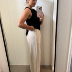 Woman taking a mirror selfie wearing a black top and natural pants.
