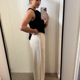 Woman taking a mirror selfie wearing a black top and natural pants.
