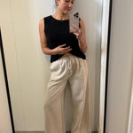 Woman taking a mirror selfie wearing a black sleeveless top and beige pants.