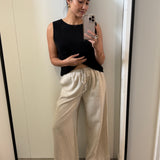 Woman taking a mirror selfie wearing a black sleeveless top and beige pants.