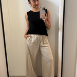 Woman taking a mirror selfie wearing a black sleeveless top and beige wide-leg pants.