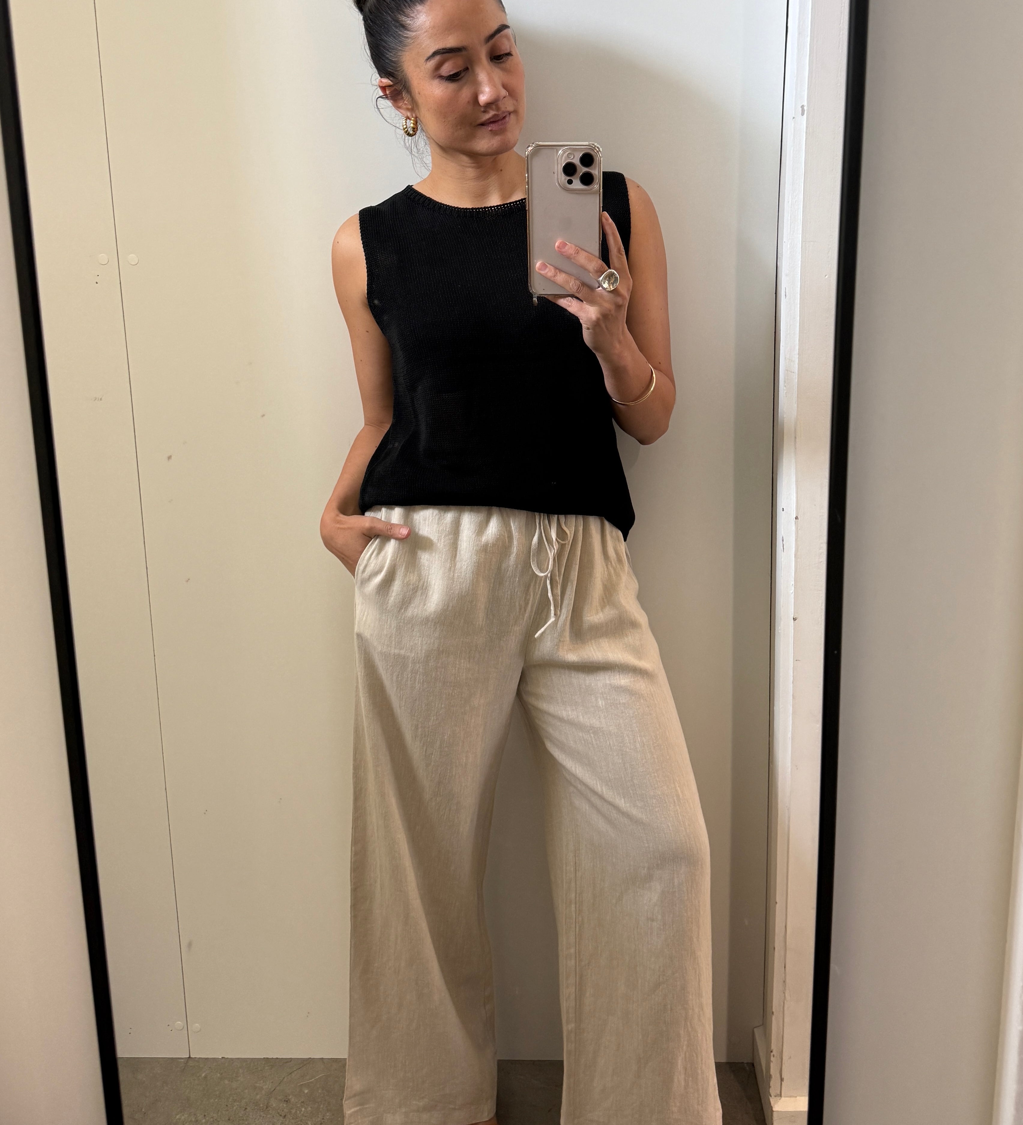 Woman taking a mirror selfie wearing a black sleeveless top and beige wide-leg pants.