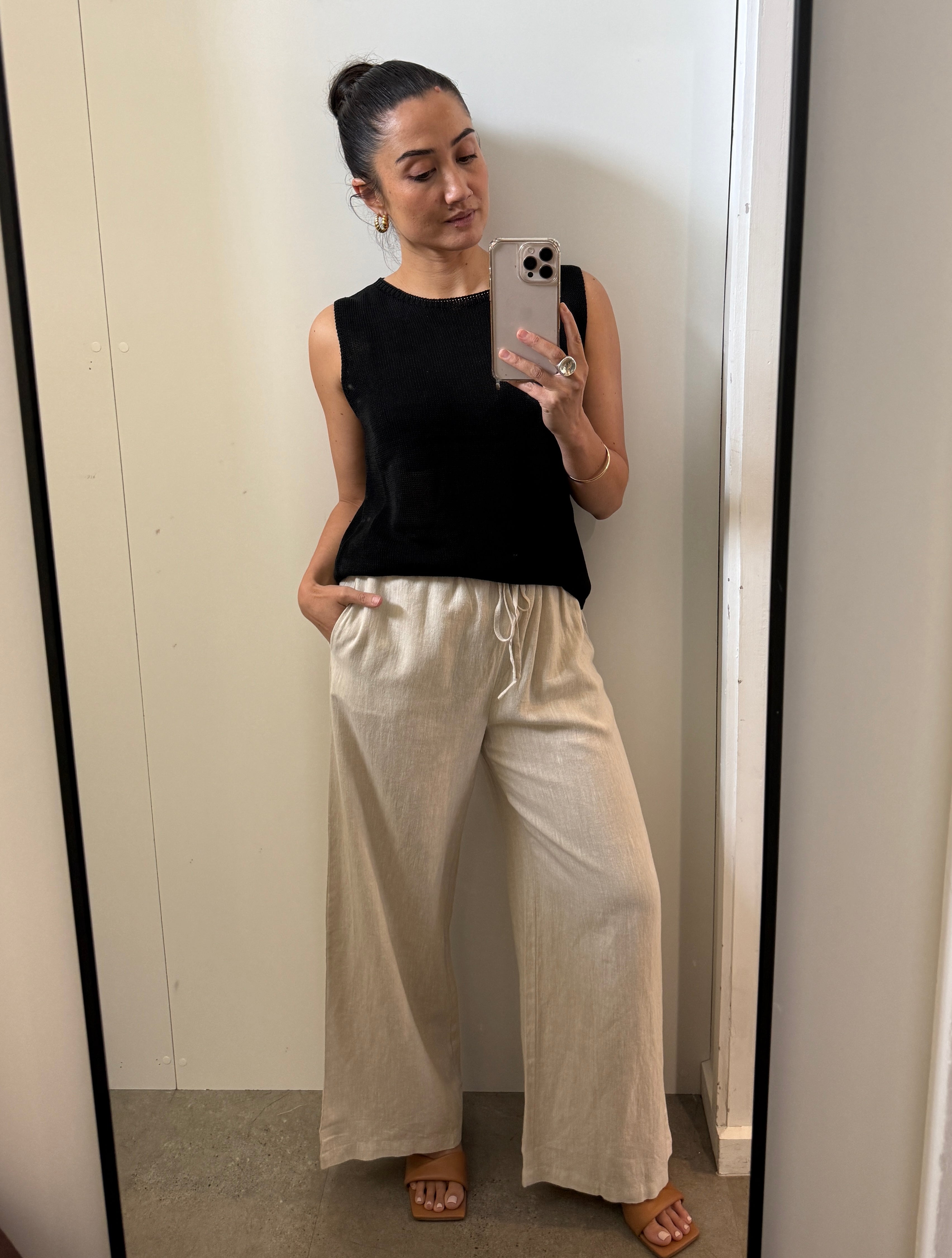 Woman taking a mirror selfie wearing a black sleeveless top and beige wide-leg pants.