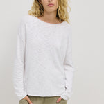 A woman wearing a white long-sleeved top with a relaxed fit, standing with hands in pockets.
