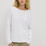 A woman wearing a white long-sleeved top with a relaxed fit, standing with hands in pockets.