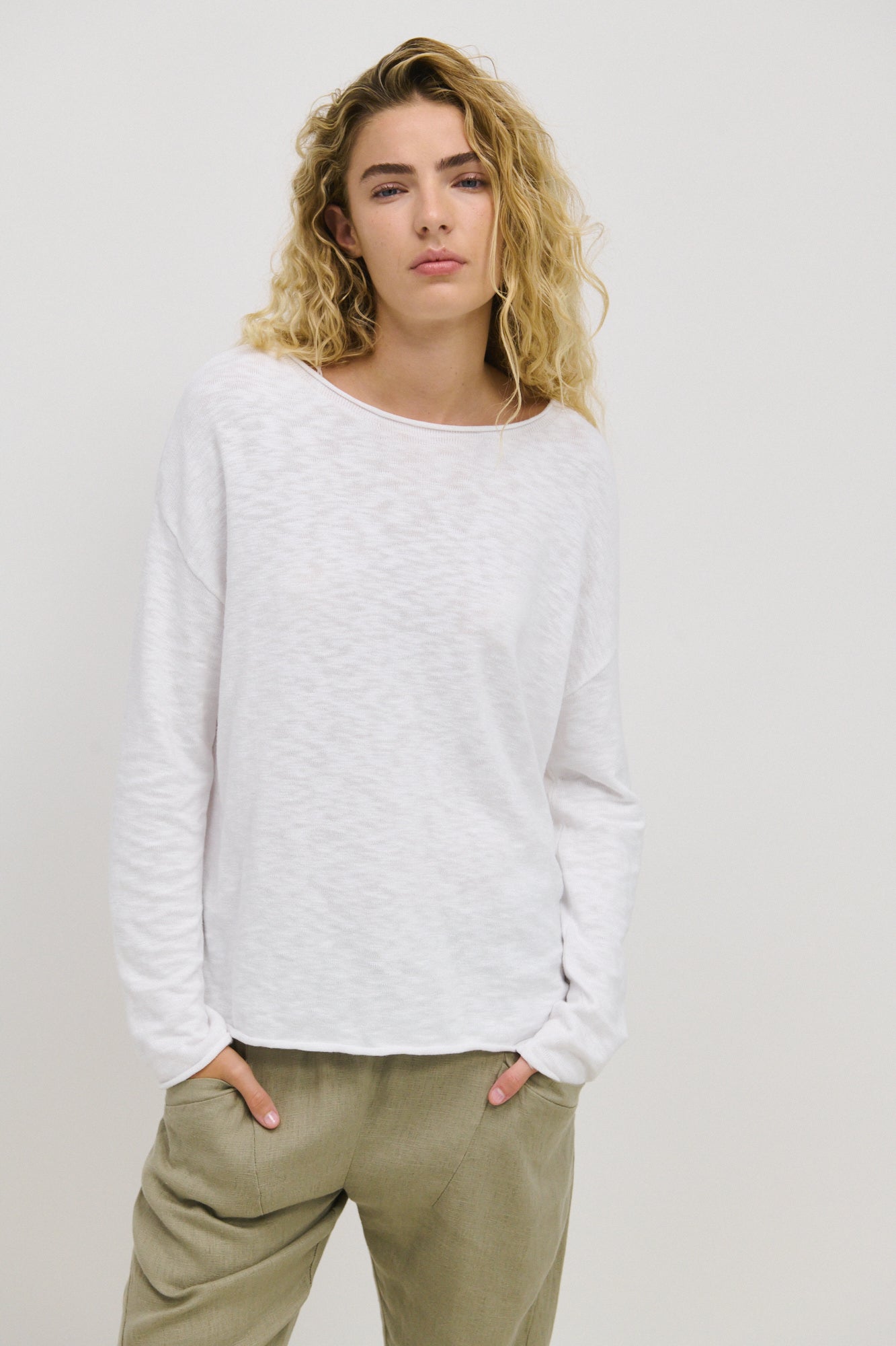 A woman wearing a white long-sleeved top with a relaxed fit, standing with hands in pockets.