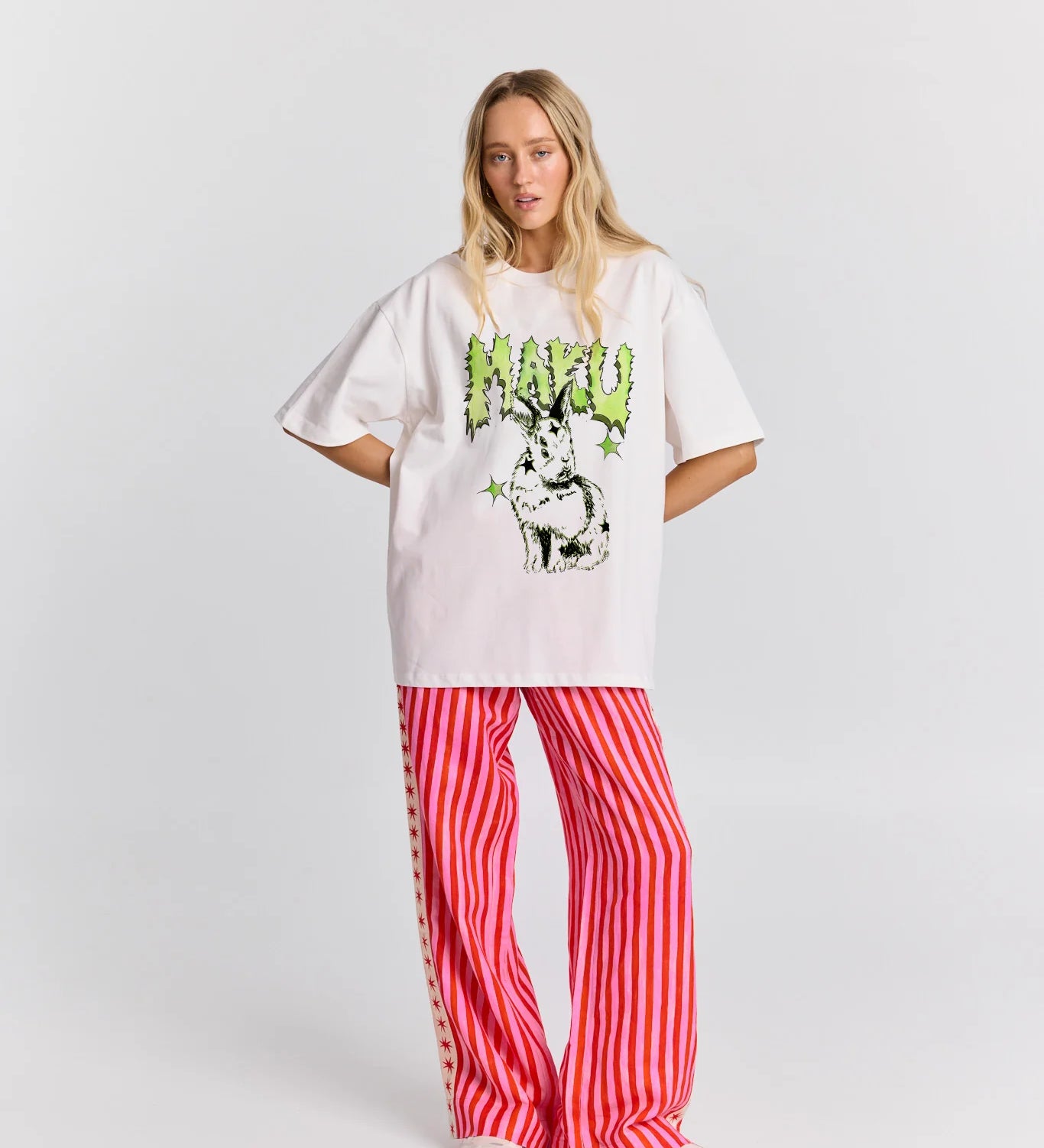 Person wearing a white oversized t-shirt with a graphic design and red striped pants on a white background