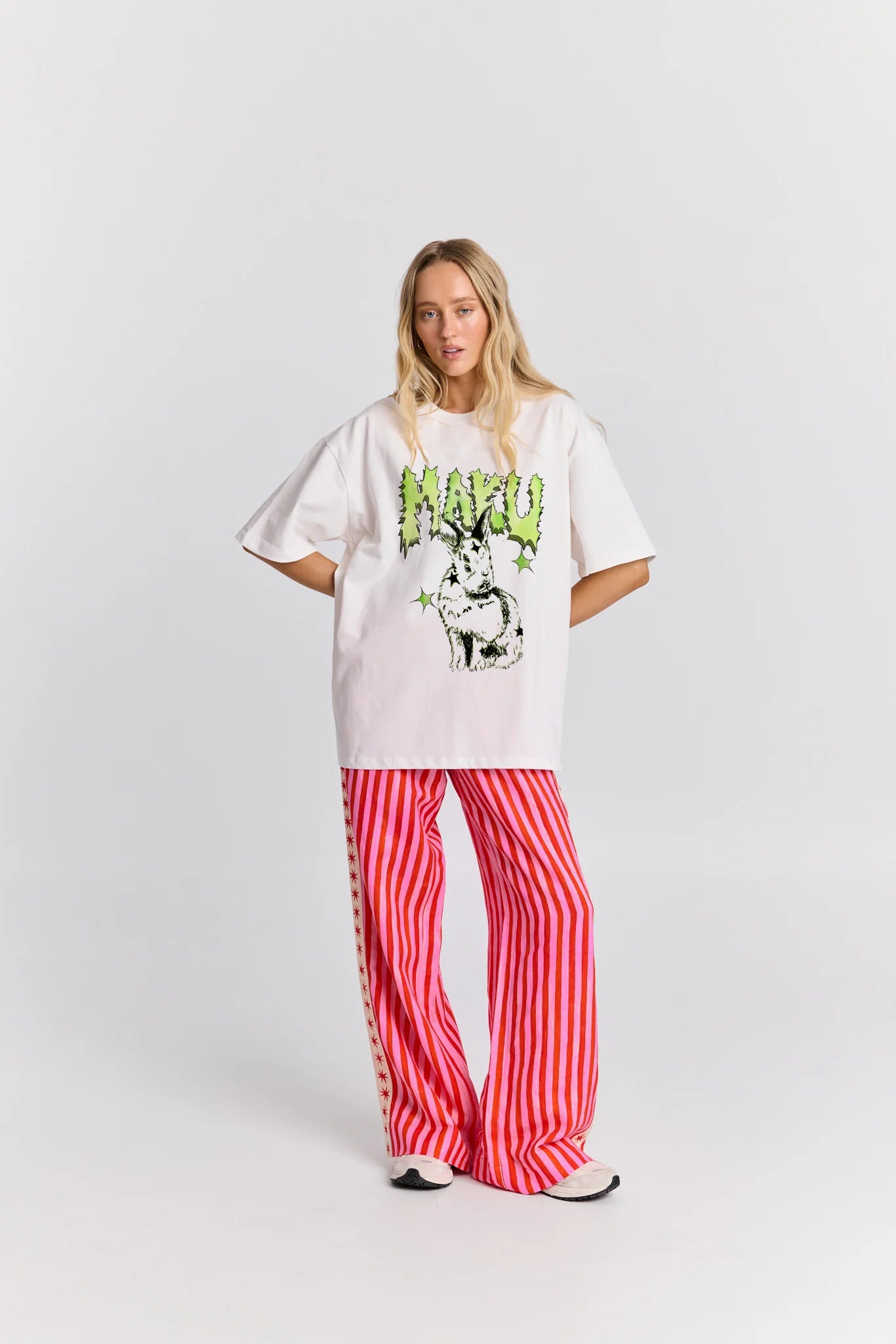 Person wearing a white oversized t-shirt with a graphic design and red striped pants on a white background