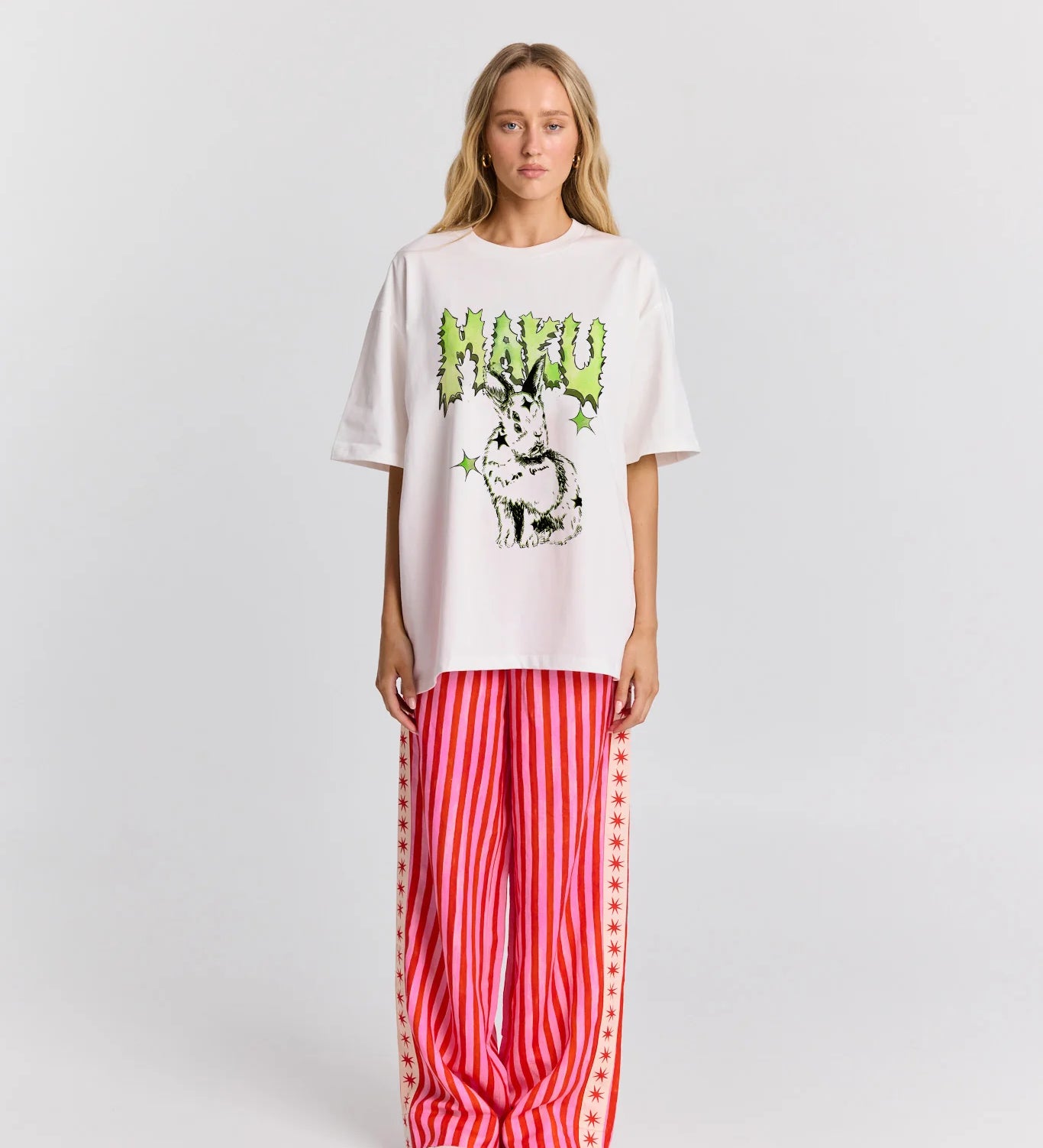 Person wearing a white oversized t-shirt with graphic design and red striped pants on a white background