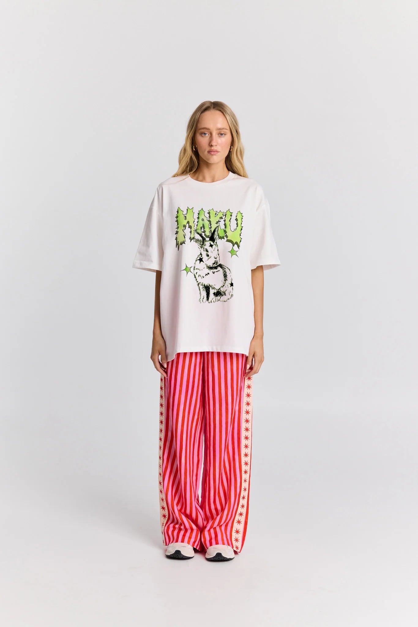 Person wearing a white oversized t-shirt with graphic design and red striped pants on a white background