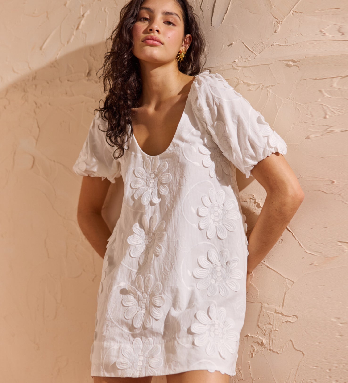 Woman wearing a white floral dress against a beige wall