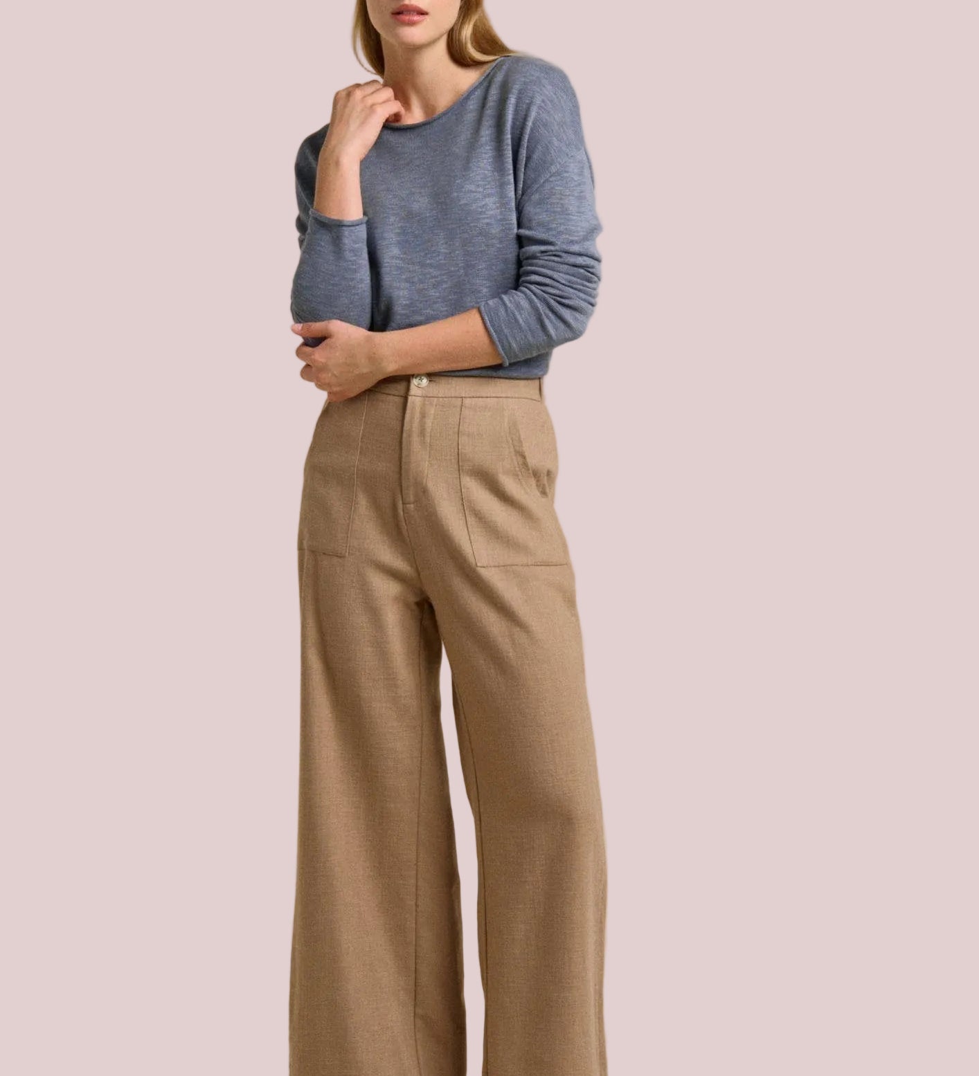 Woman wearing a blue sweater and beige pants on a beige background