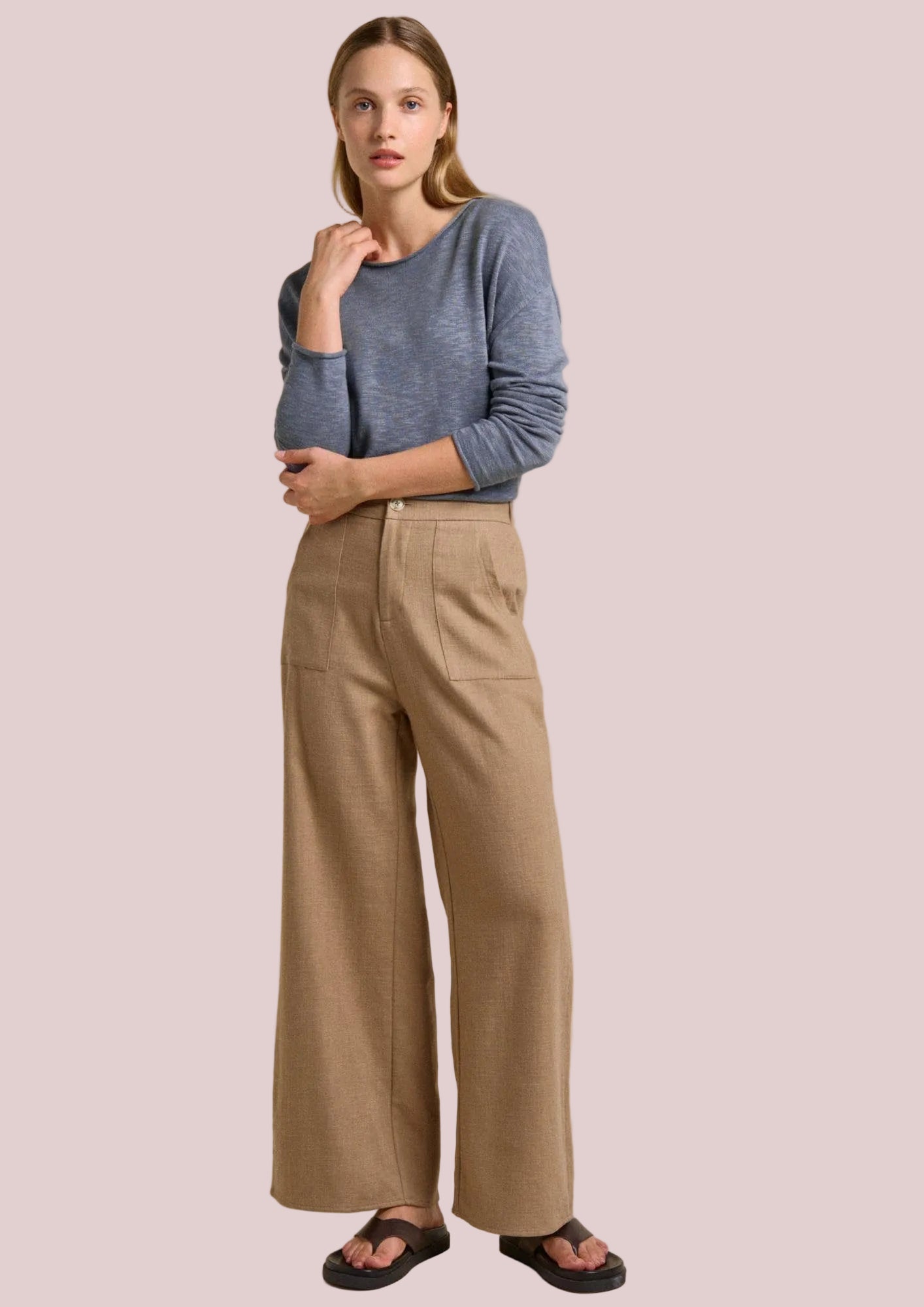 Woman wearing a blue sweater and beige pants on a beige background