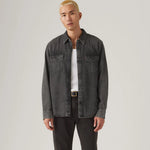 Man wearing a dark denim jacket over a white shirt on a plain background