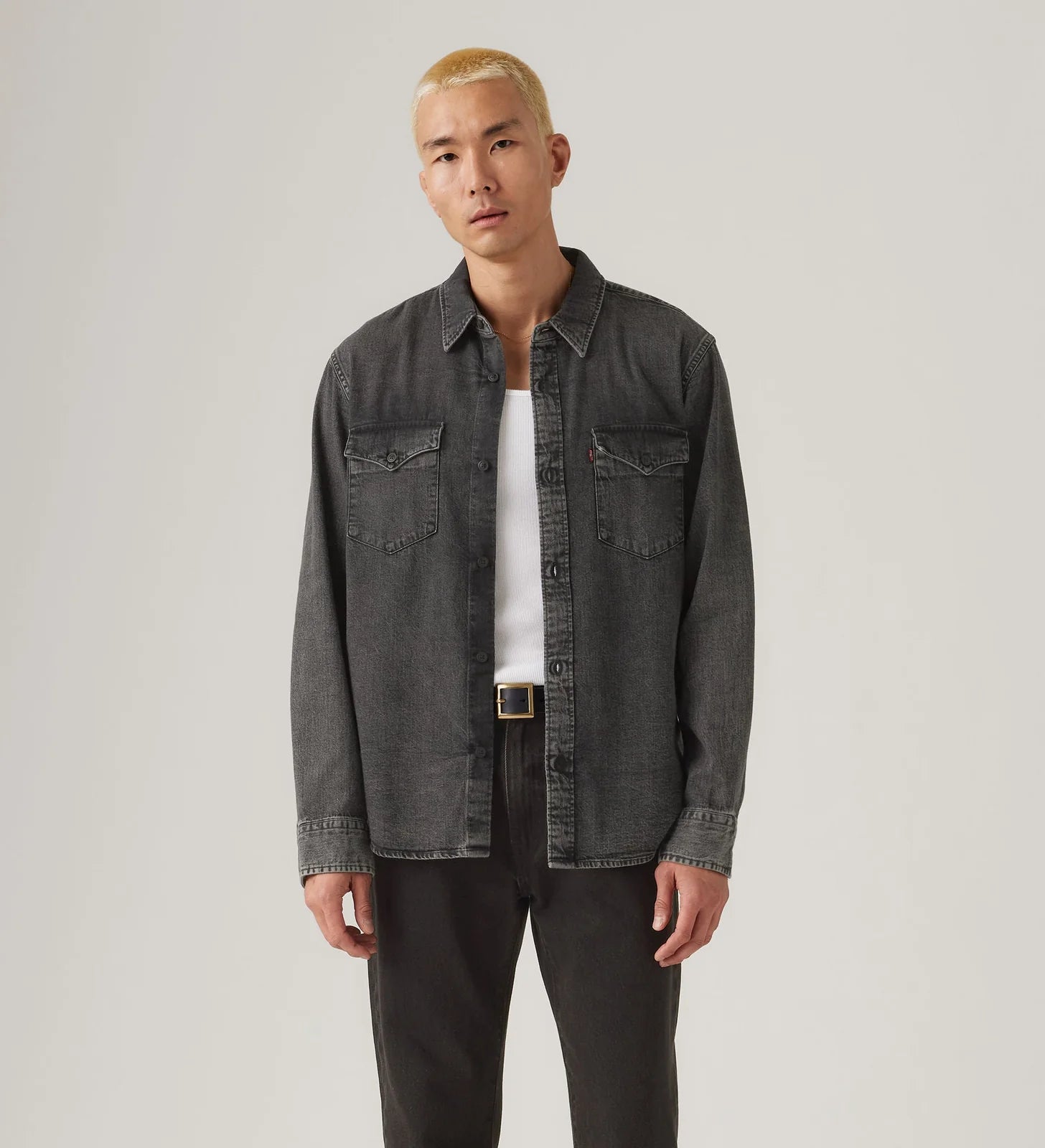 Man wearing a dark denim jacket over a white shirt on a plain background