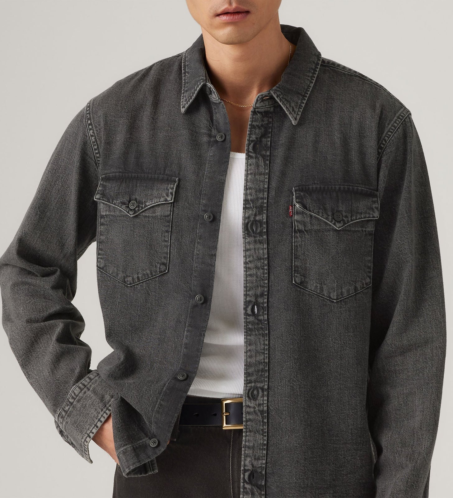 Person wearing a dark denim shirt over a white t-shirt on a plain background