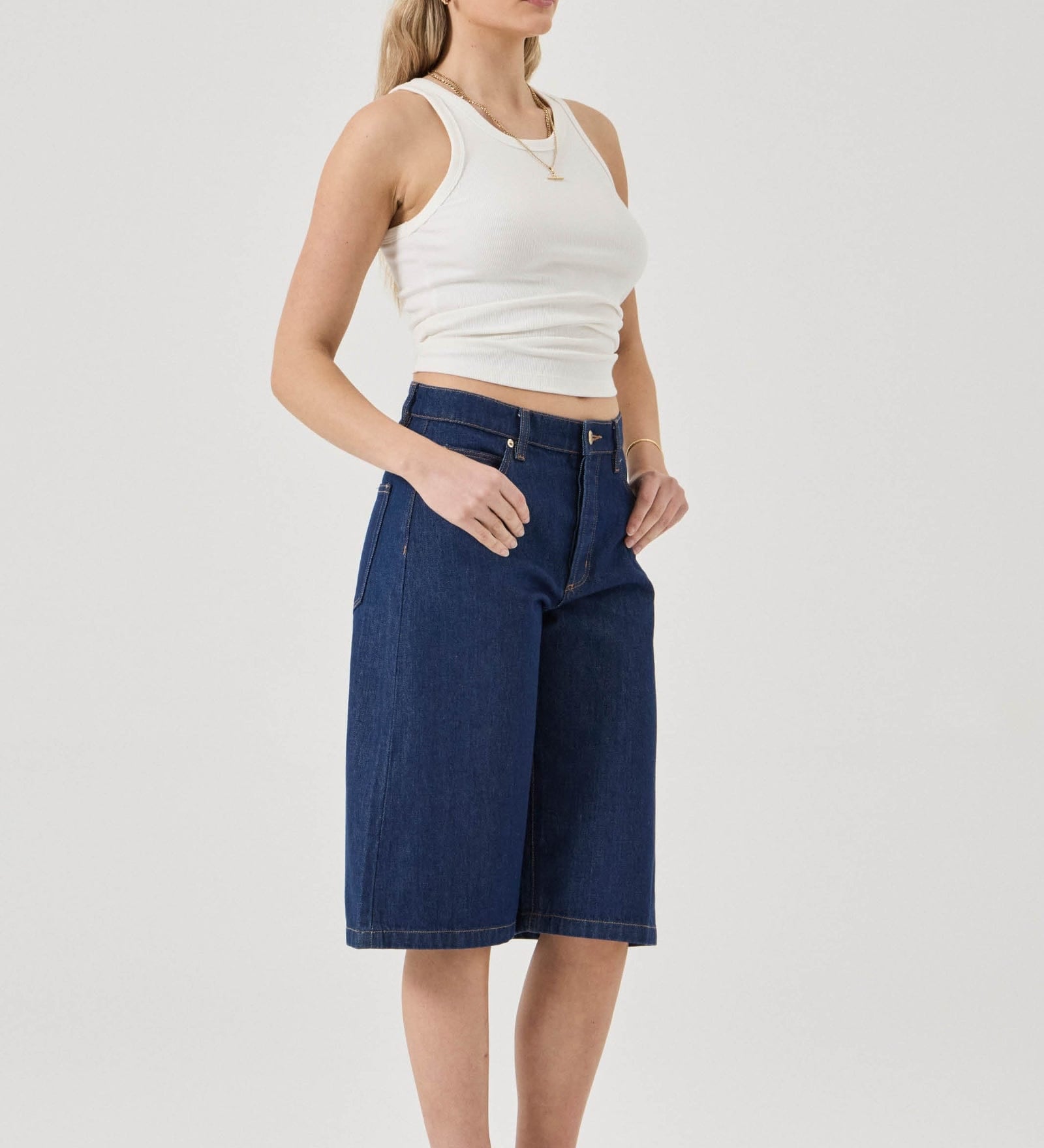 Woman wearing a white tank top and blue denim shorts on a plain background