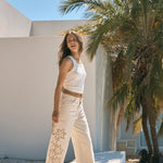 Woman in a white outfit standing in front of a palm tree and white building.