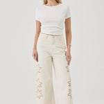 Woman wearing a white top and beige pants with star patterns on a white background