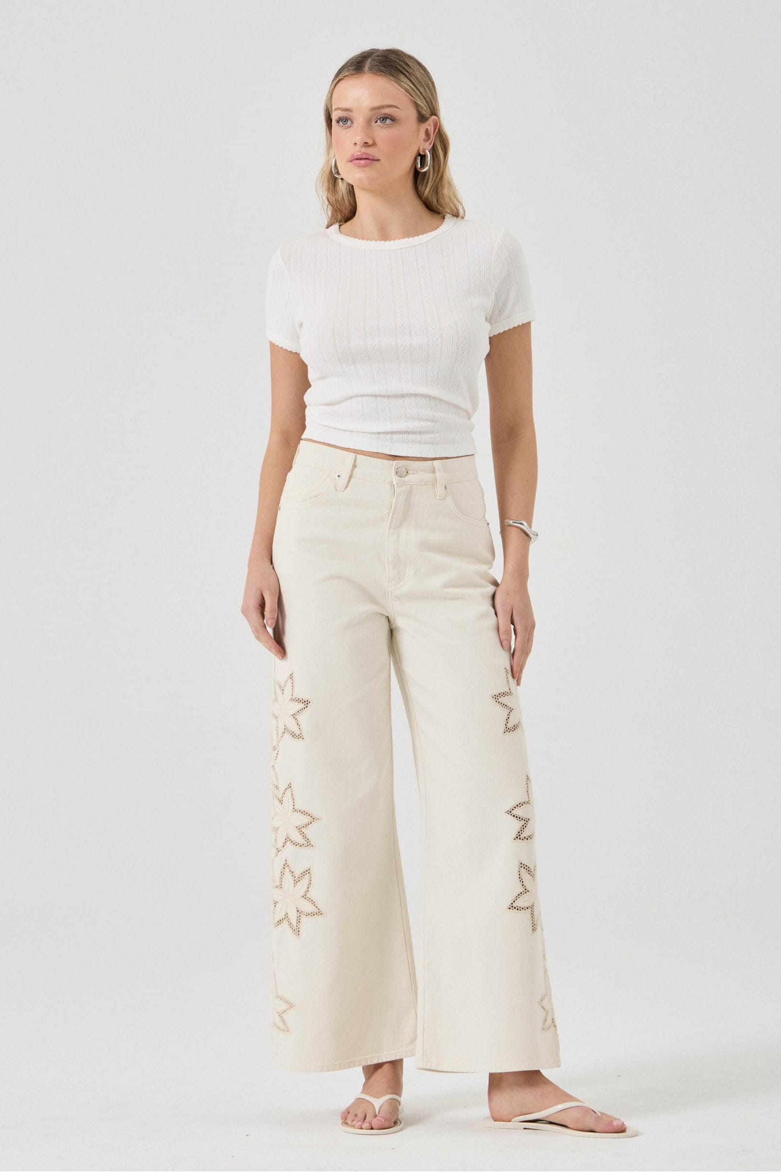 Woman wearing a white top and beige pants with star patterns on a white background