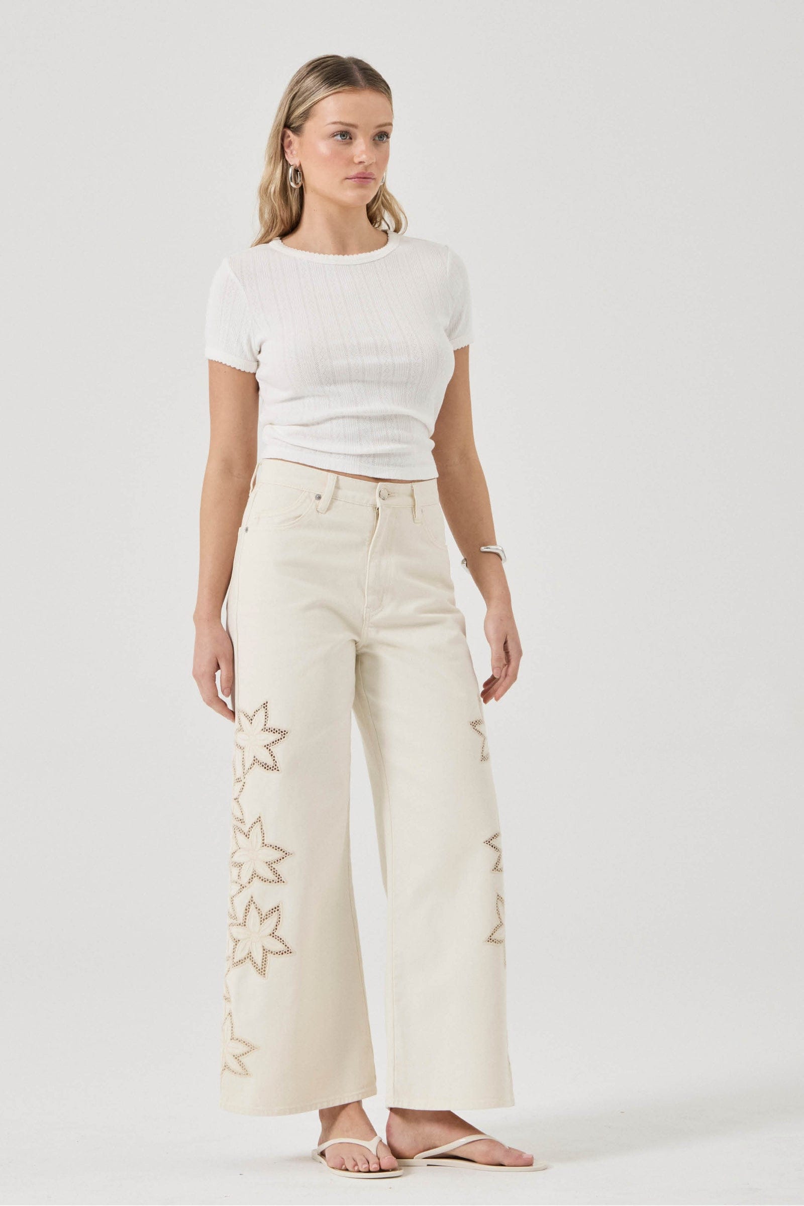 Woman wearing a white t-shirt and cream pants with star designs on a white background