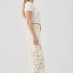 Woman wearing a white t-shirt and cream pants with star patterns on a plain background